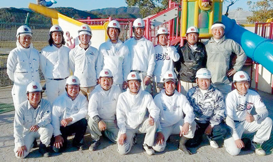 20回目のボランティアとなった高知県高知市の芸術学園幼稚園の前で記念撮影をする塗魂ペインターズの親方メンバーたち。ボランティア前日までに、高知県の沢田塗装店が延べ約16人工をつかい下地処理をしてくれていたという
