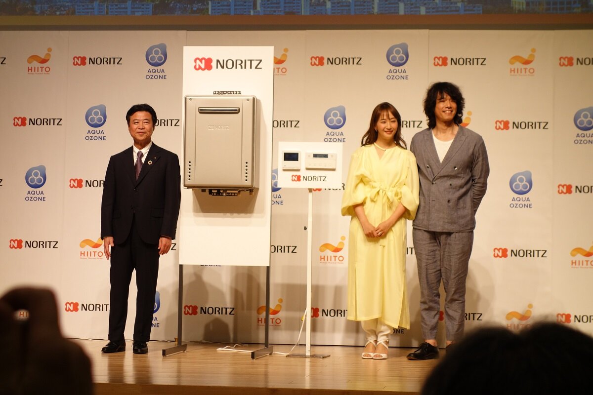 ノーリツ 　左から腹巻知社長、特別ゲストの藤本美貴氏、庄司智春氏。会見ではノーリツ公認の「アツアツ夫婦」に任命され、「おふろルール」や夫婦の「アツアツエピソード」などトークセッションが行われた。中央は新商品の給湯器。